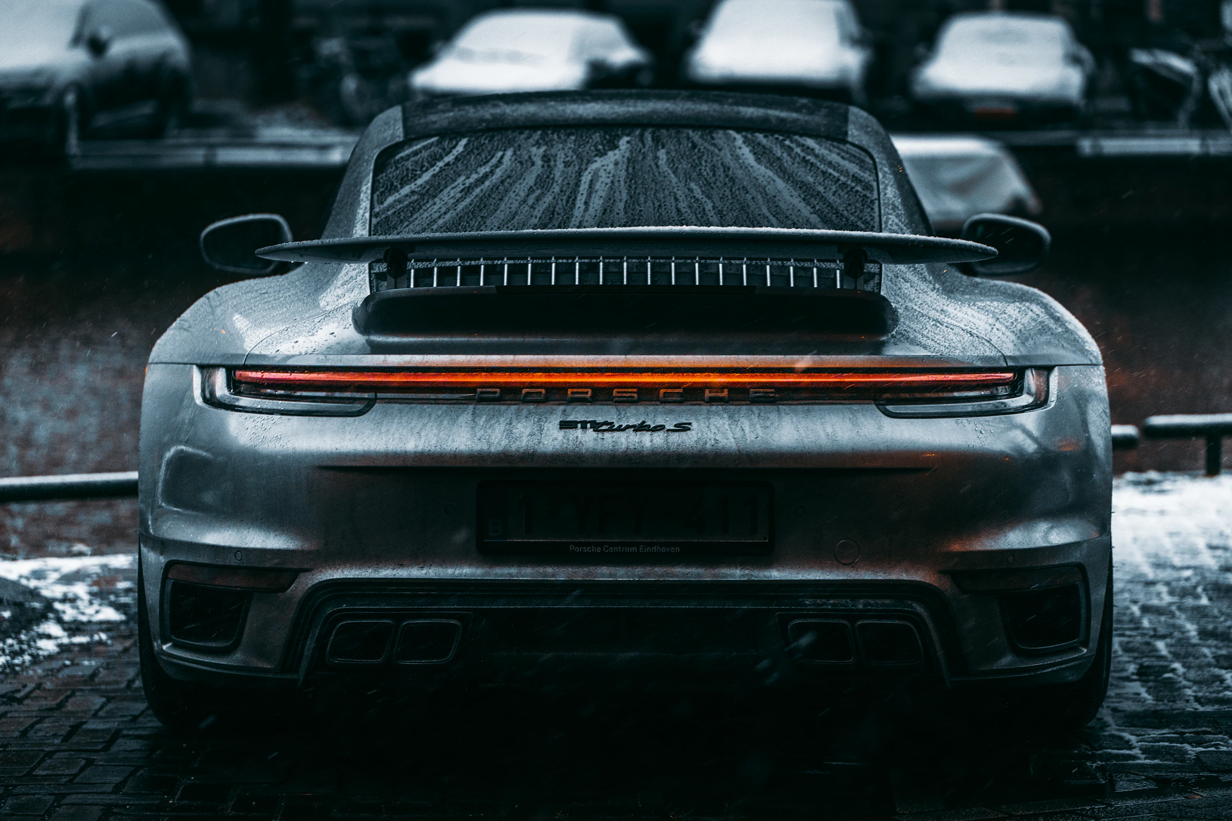 The rear of a dark sports car on wet cobblestones.