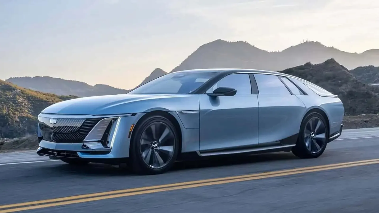 A light blue Cadillac Celestiq electric sedan driving on a two-lane mountain road at dusk