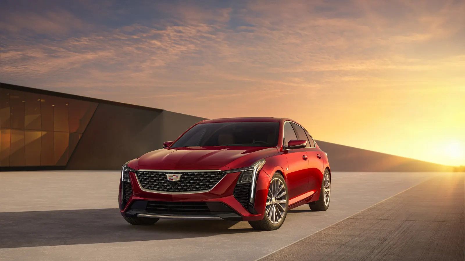 A red 2026 Cadillac CT5 sedan parked on a concrete plaza beside a low building at sunset