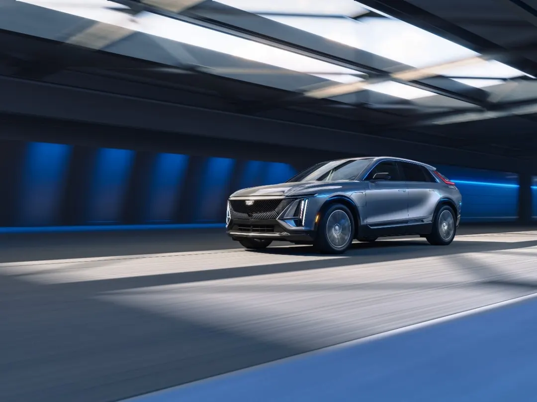 A silver Cadillac Lyriq electric SUV driving through a brightly lit tunnel with blue accent lighting