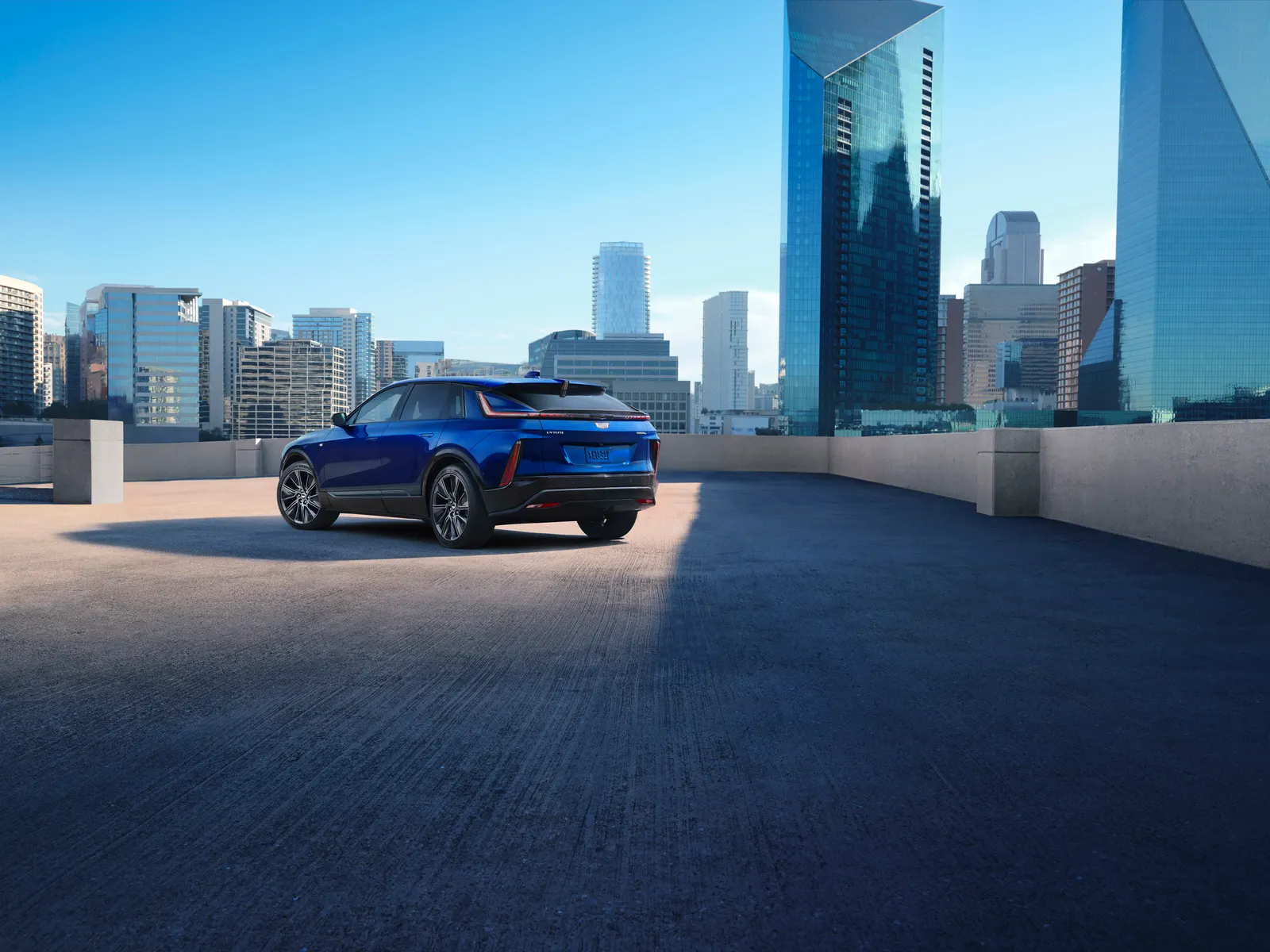 A blue 2026 Cadillac Lyriq parked on a rooftop deck with glass office towers behind it