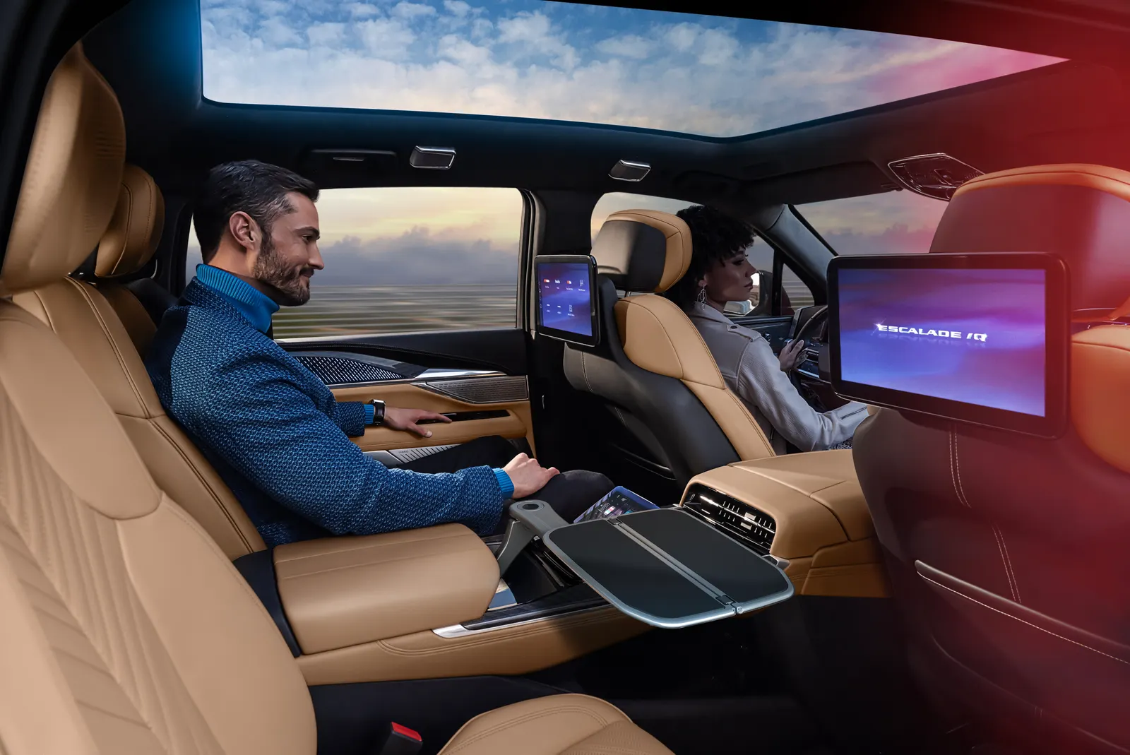 A man in the second row and a woman at the wheel inside a Cadillac Escalade IQ with tan leather seats and seatback screens