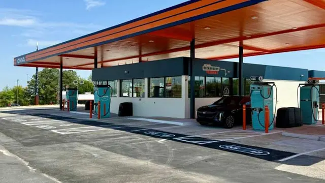 A black Cadillac electric SUV parked at an IONNA Rechargery with teal charging dispensers under an orange and blue canopy