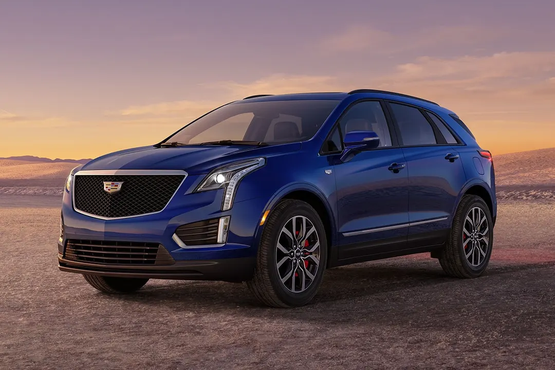 A dark blue 2026 Cadillac XT5 Sport crossover parked on a desert flat at sunset, seen from the front three-quarter angle