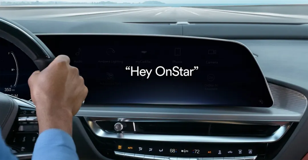 A driver's hand on the steering wheel of a Cadillac Lyriq while the curved dashboard screen shows the words Hey OnStar