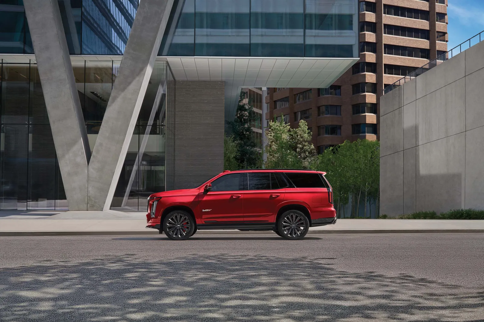 Side view of a red Cadillac Escalade-V with dark wheels parked on a city street in front of glass office buildings