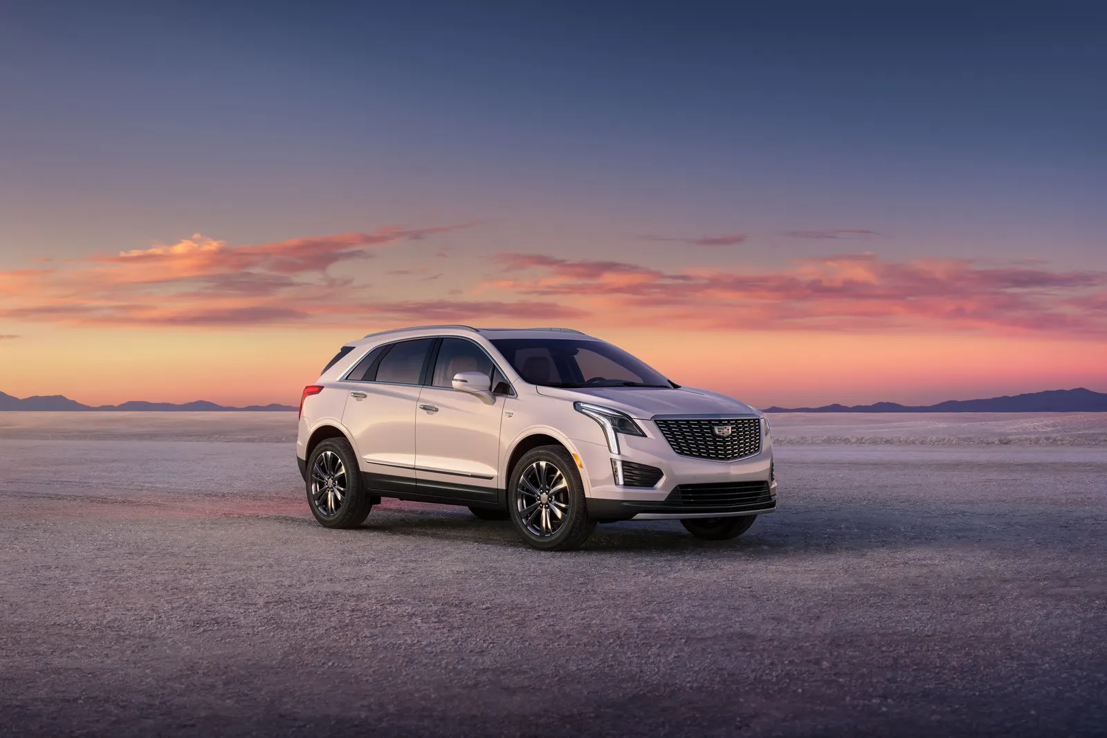 A white 2025 Cadillac XT5 parked on a flat desert plain under an orange and purple sunset sky