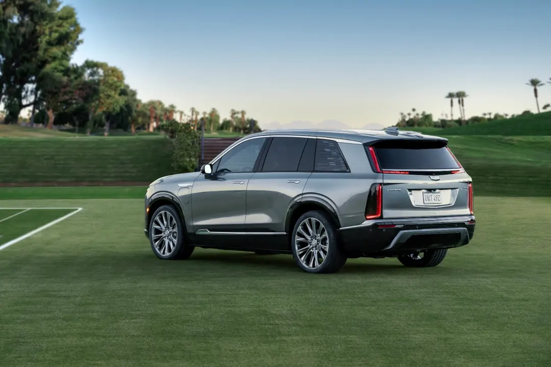 Rear three-quarter view of a silver 2026 Cadillac Vistiq three-row electric SUV parked on a lawn at dusk