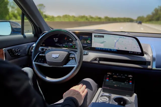 Driver's view inside a 2026 Cadillac Vistiq on a highway with Super Cruise engaged, hands off the steering wheel and the navigation map on the curved display